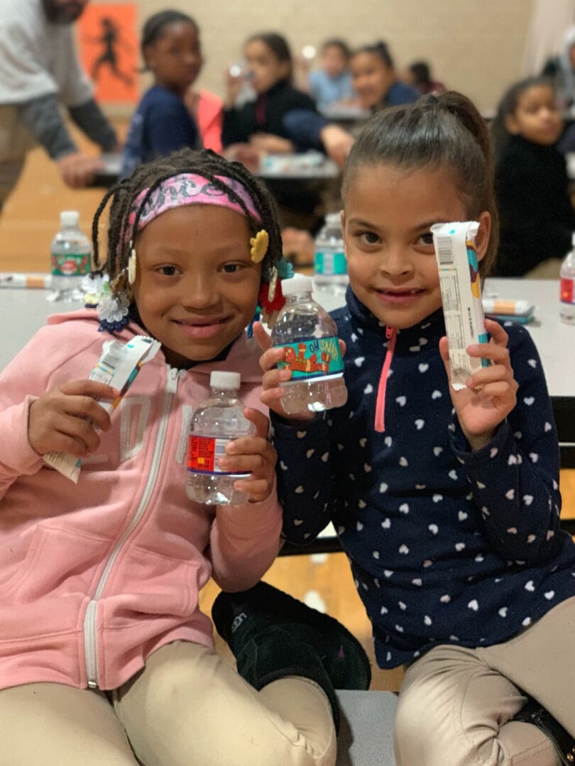 Two young girls holding water bottles and a packaged snack